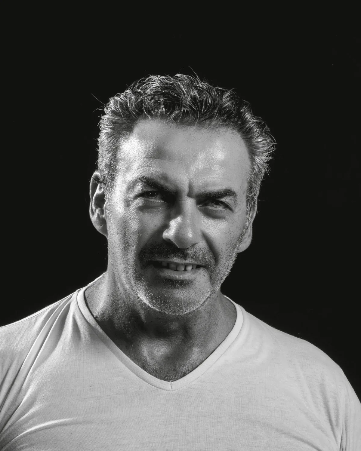 Patrick Chekkat, photographe, en t-shirt blanc, portrait en noir et blanc sur fond noir